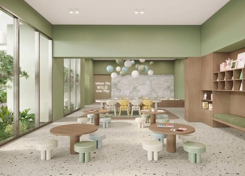 Modern childcare classroom with sage green walls, wooden curved tables, small seating, large windows, and natural light