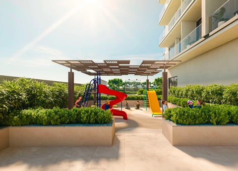 Modern rooftop playground with red and yellow slides, wooden pergola, and green hedges surrounding the play area